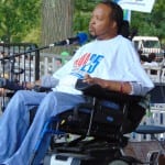 A person in a wheelchair speaks into a microphone.
