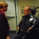 A person in a maroon suit speaks to a person in a wheelchair.