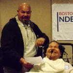 Person standing next to a person in a wheelchair who is speaking into microphone.