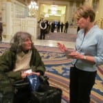 A person in a power wheelchair speaks with a person in a powder blue suit jacket.