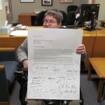 Person in a wheelchair holds a signed letter to the Chairperson.