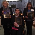 Three people, one in a wheelchair, present their awards at event.