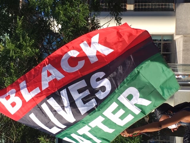 A flag consisting of three horizontal lines, one red, one black and one green, reads BLACK LIVES MATTER in large white letters.