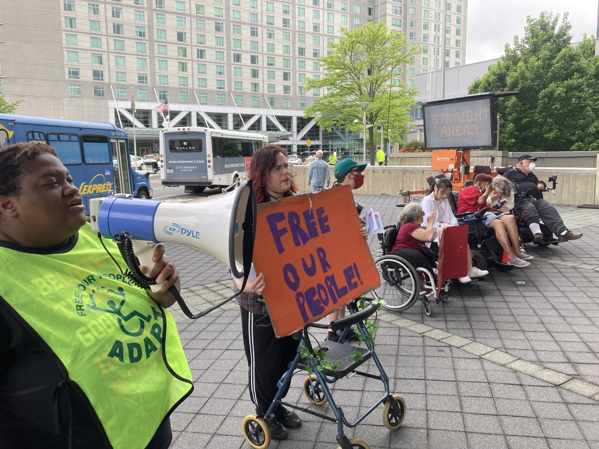 Disability Advocates protesting in Boston holding signs and one person with a megaphone.